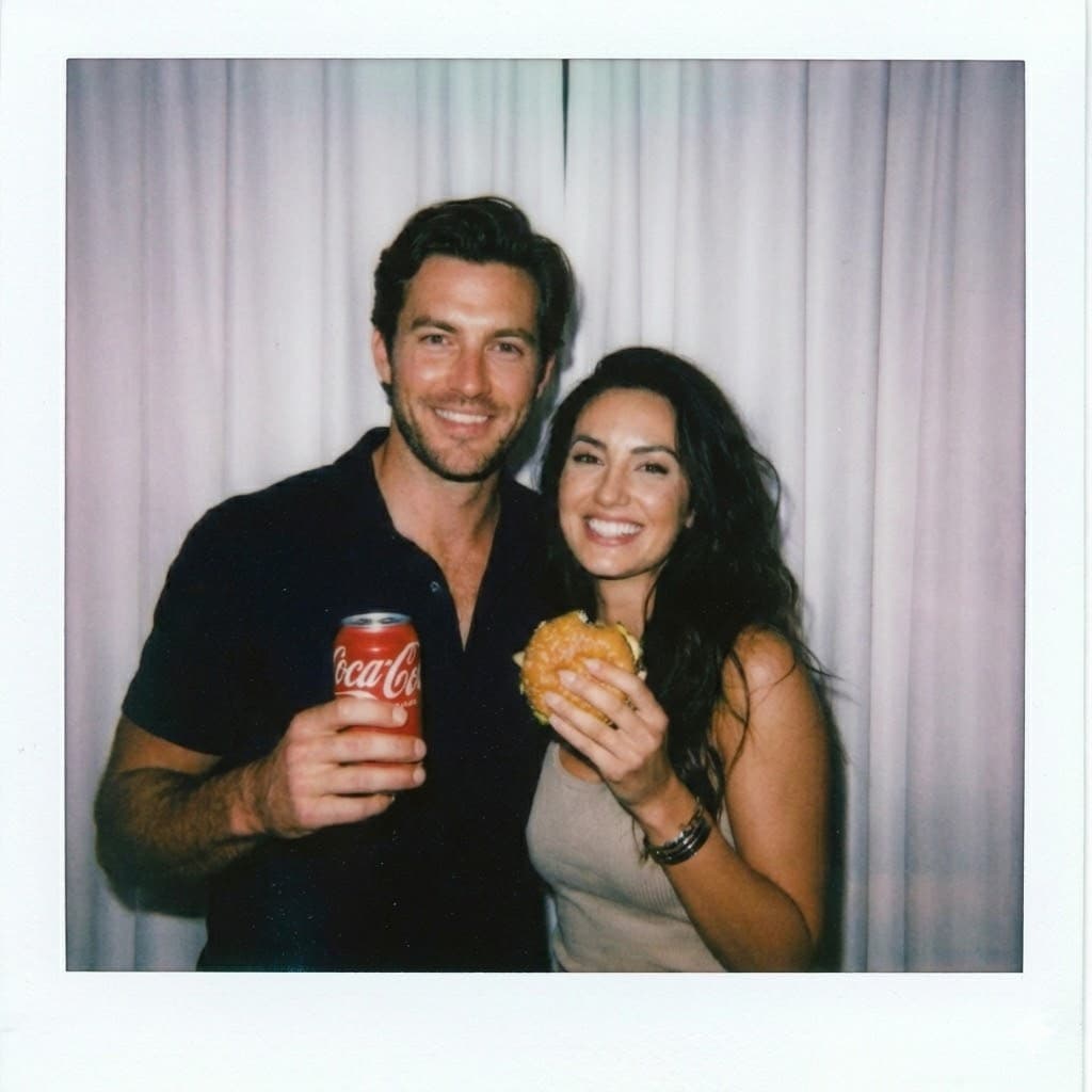 Nano Banana generated image: Take a photo taken with a Polaroid camera. The photo should look like an ordinary photograph, without an explicit subject or property. The photo should have a slight blur and a consistent light source, like a flash from a dark room, scattered throughout the photo. Don't change the face. Change the background behind those two people with white curtains. With that boy and me make a cute poses. Make the boy holding a red coca cola can and girl a burger.