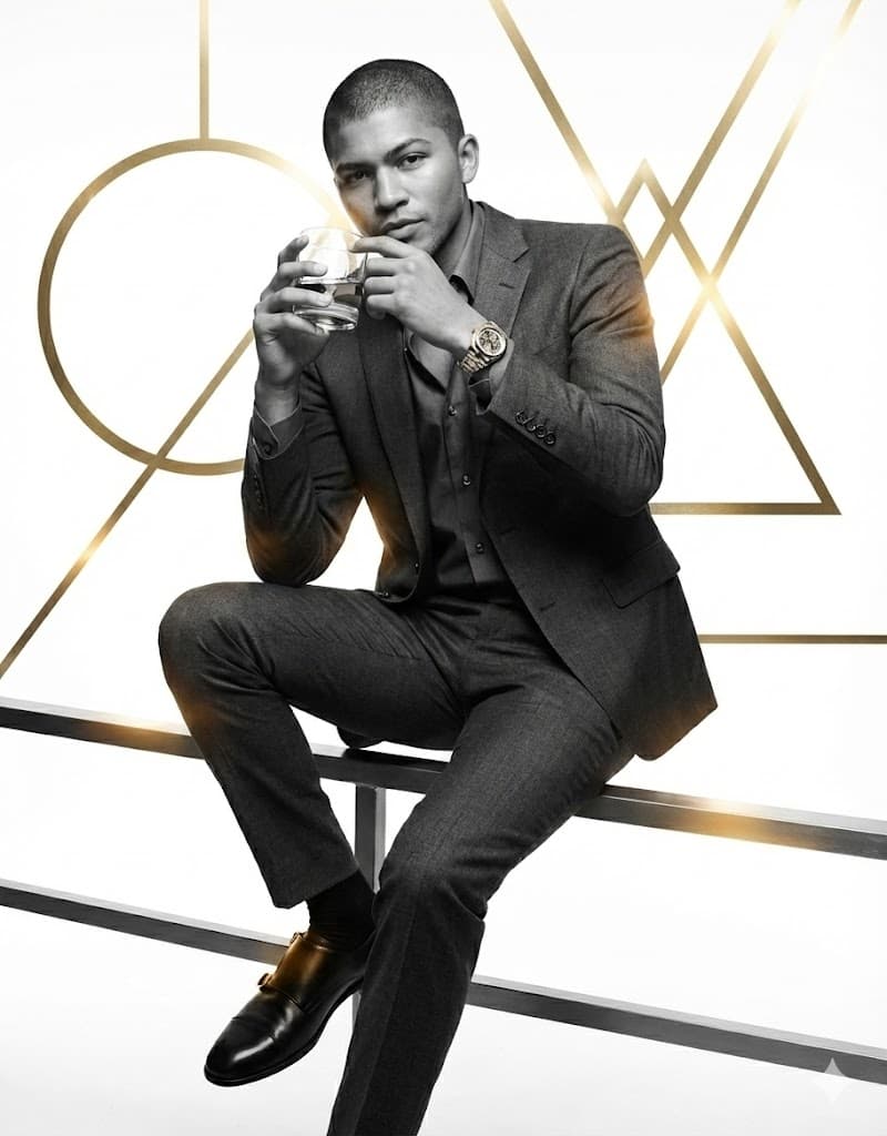 Nano Banana generated image: Generate a B&W picture of me following the prompt:
Character
A strong, athletic man - as per my picture - in his late 30s sits casually on a railing, one arm on his knee, the other raised near his face holding a glass of bourbon.
Clothing and Accessories
He wears a grey charcoal suit with a matching shirt, top button open, a silver and gold skeleton Rolex watch. black shoes with gold double buckle
Lighting Detail
Warm yellow and red reflections move across his suit and face, adding depth and a cinematic metallic glow.
Background
Clean white background with pure gold geometric shapes — circles, triangles, and lines — intersecting through the frame, blending modern design with luxury photography.
Style / Mood
Cinematic, masculine, modern. Editorial minimalism with a tone of quiet wealth and strength.